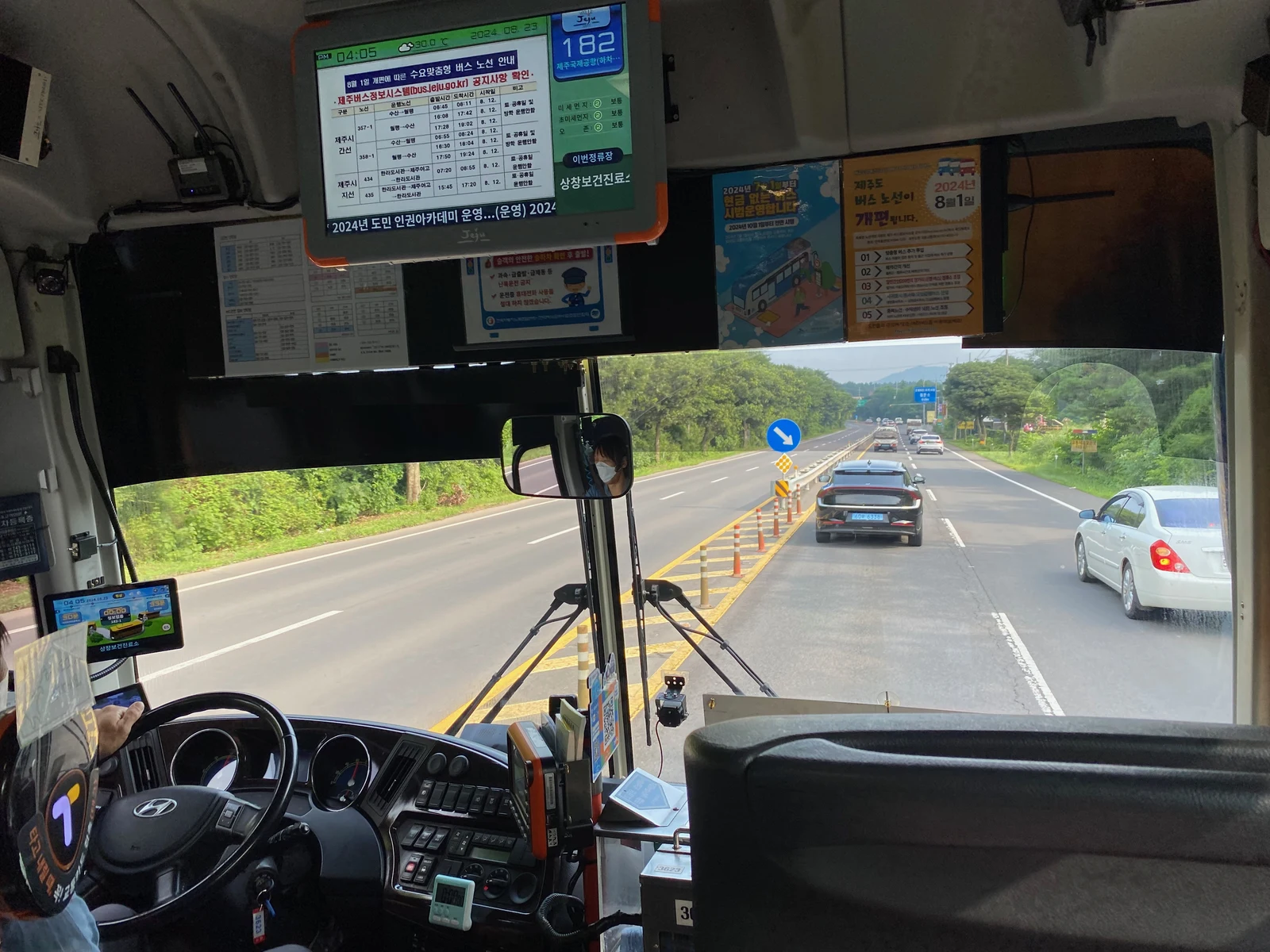 A road viewed from a Jeju bus on 23 August 2024. The interior display shows route 182 and the Sangchang public health clinic stop.