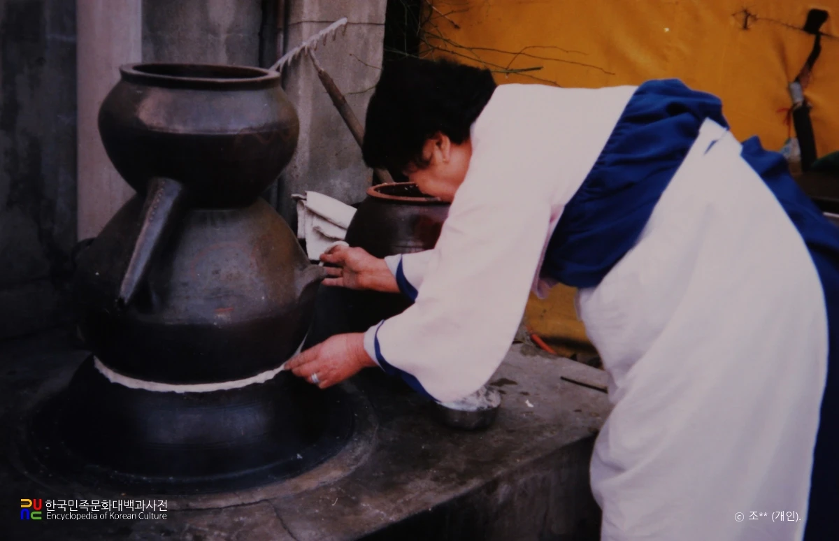 Hands working at the joint between a pot and a traditional still