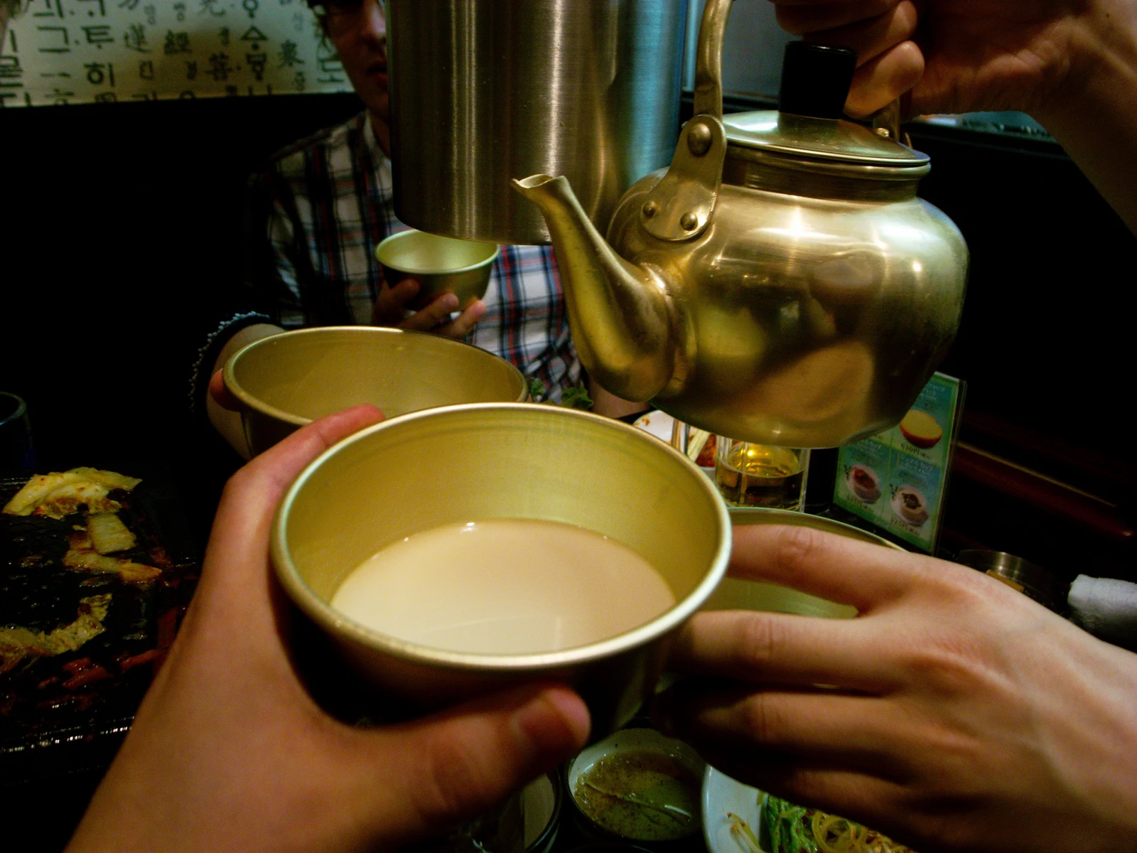 Cloudy makgeolli being poured from a kettle into a small cup