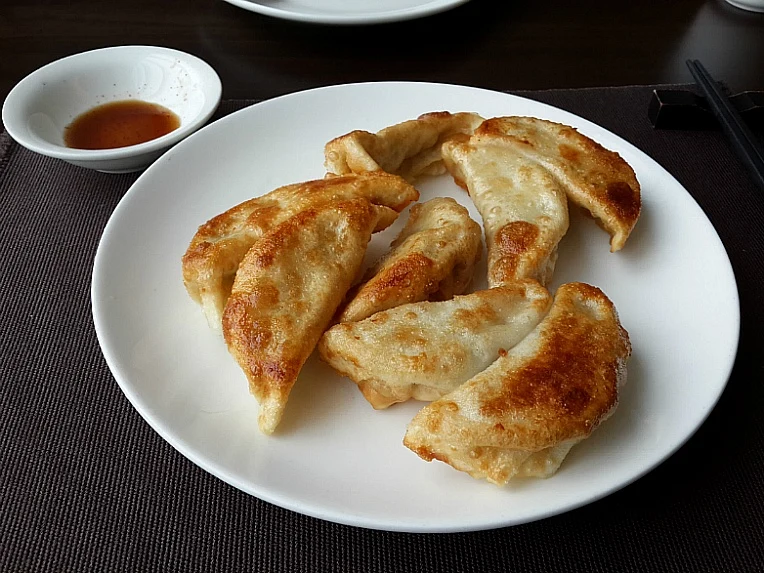 Browned dumplings on a white plate beside a small sauce bowl