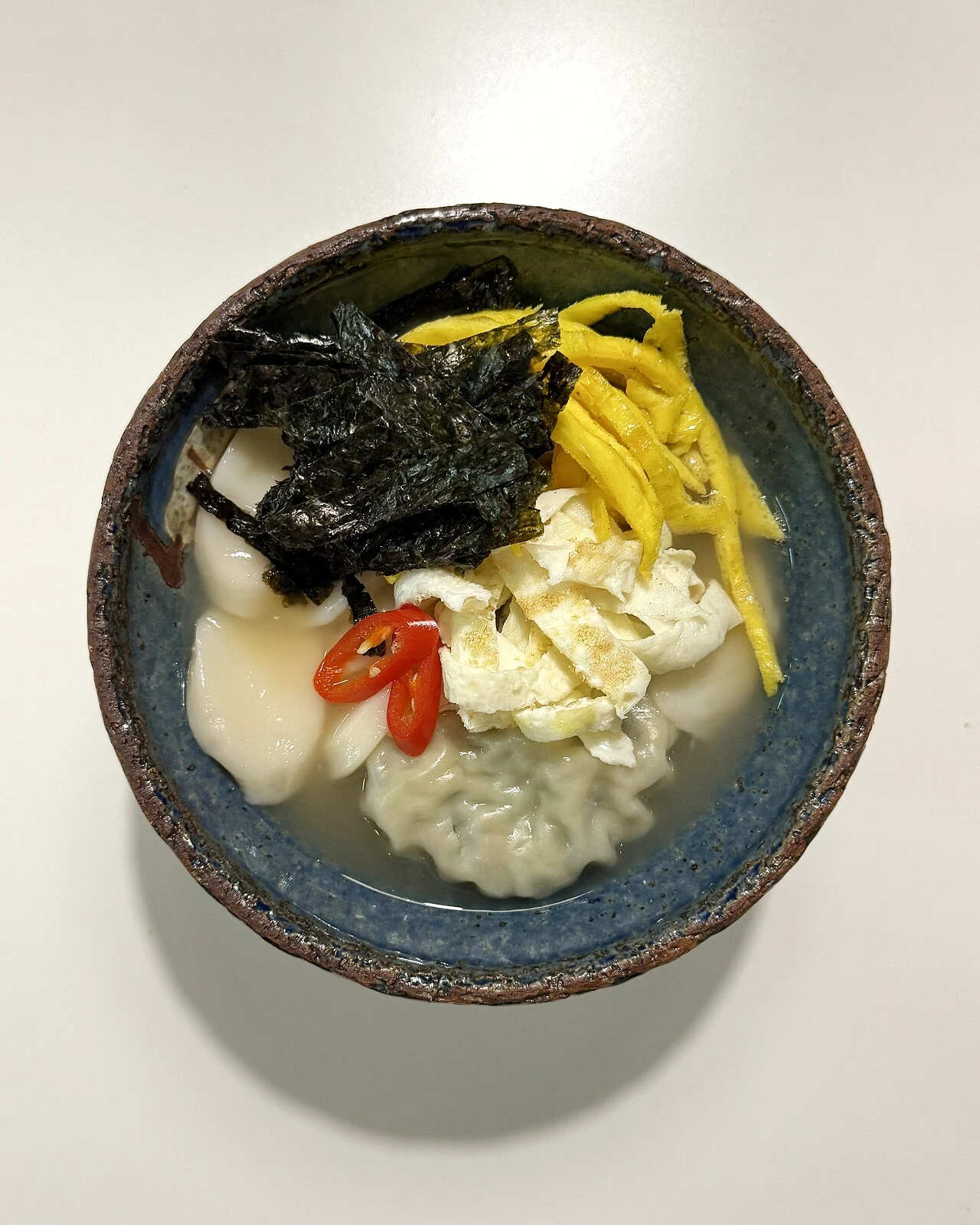 Rice-cake and dumpling soup topped with seaweed and egg
