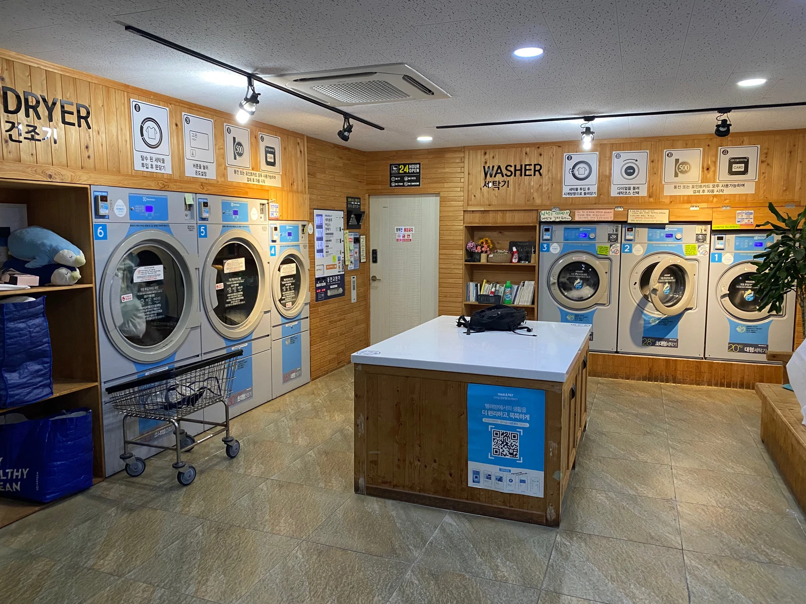 A laundromat in Jeju on August 24, 2024, with dryers on the left, washers on the right and a central worktable. Photo by Sgroey.