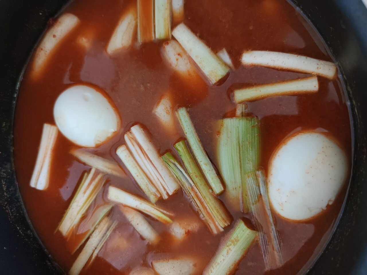 Cakes, scallions and two boiled eggs in a black pot